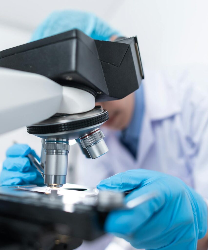 Close-up of a scientist examining samples under a microscope in a lab setting.